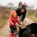 Dad helps son ride a bike on a path with family and dog, capturing a joyful outdoor moment.