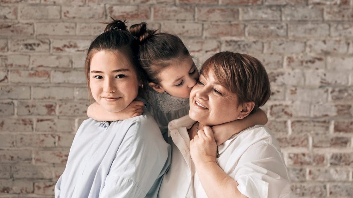 A warm family portrait of a mother with her two daughters sharing affection and smiles.