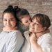 A warm family portrait of a mother with her two daughters sharing affection and smiles.